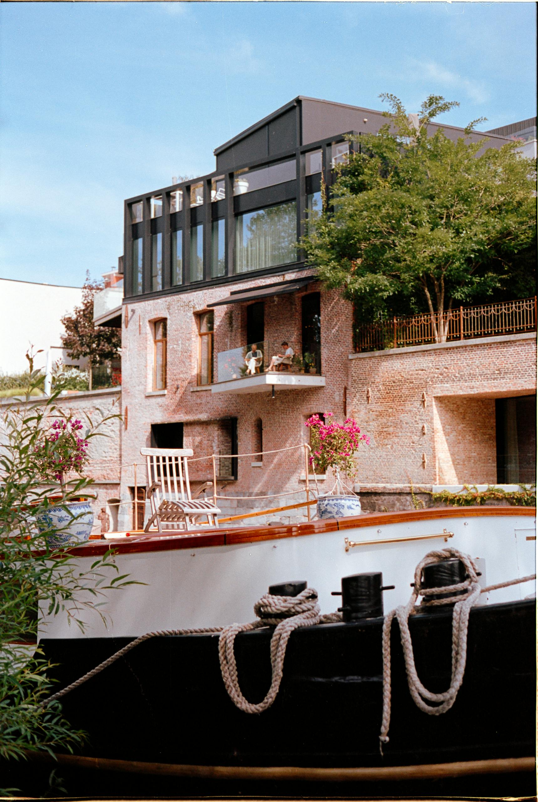 A picturesque canal house with a docked boat, flourishing greenery, and a sunny summer day.
